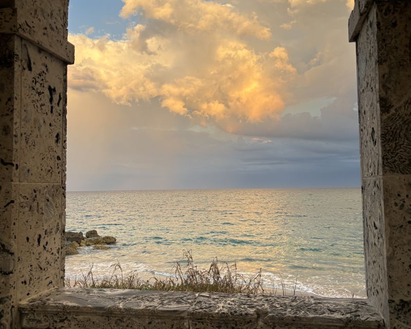 Ocean and golden clouds framed by a weathered coral-stone arch in Palm Beach County